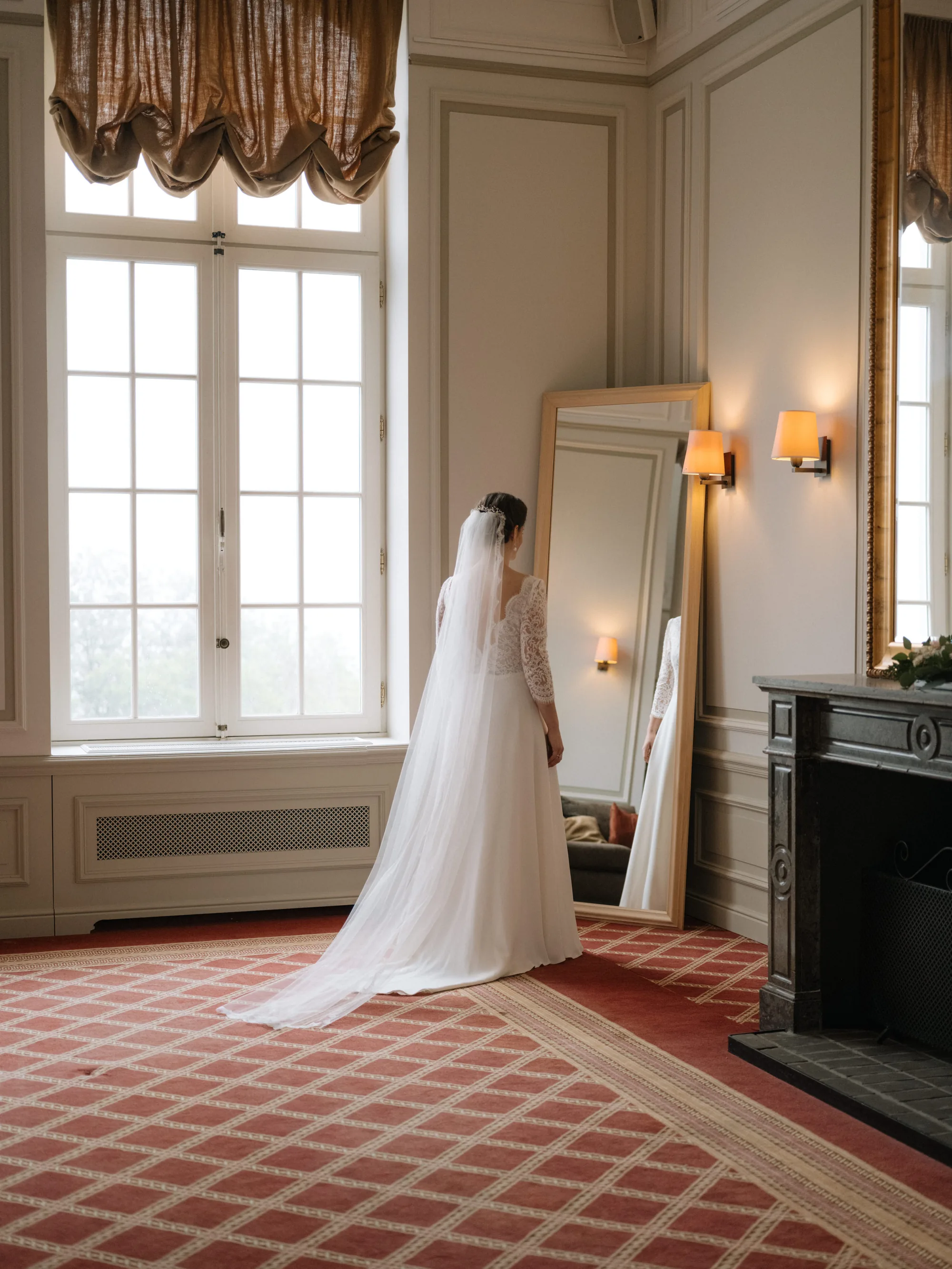 Mariée en robe blanche devant un miroir dans une pièce élégante aux tons beiges