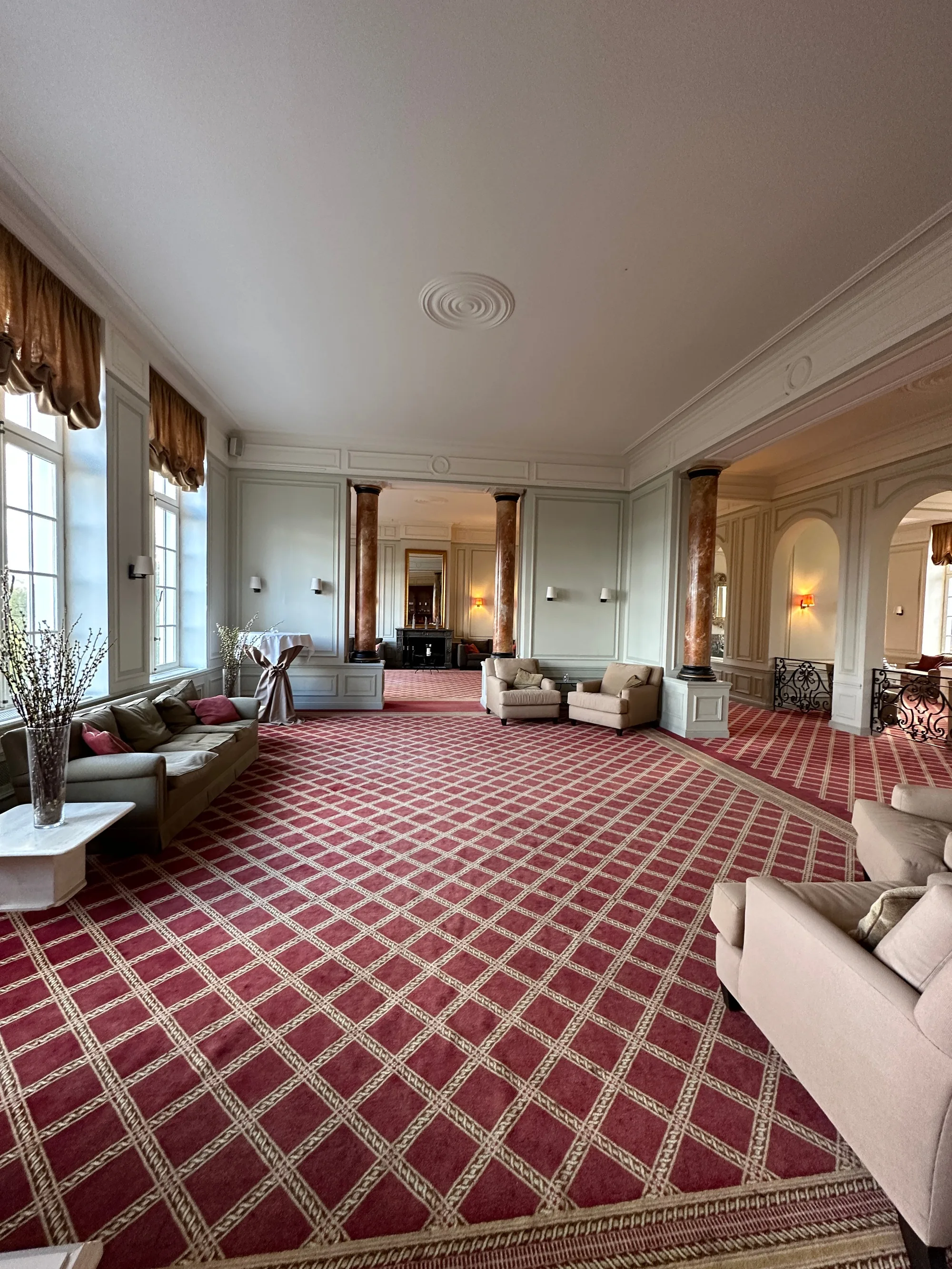 Grand salon avec tapis à motifs écossais rouges, canapés beiges et hautes fenêtres lumineuses