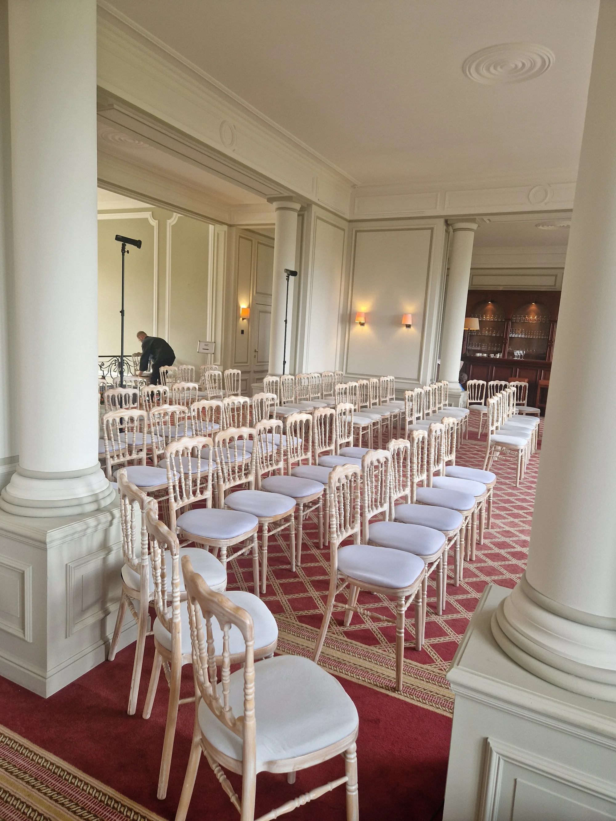 Rangées de chaises blanches alignées dans une salle élégante avec colonnes et tapis rouge