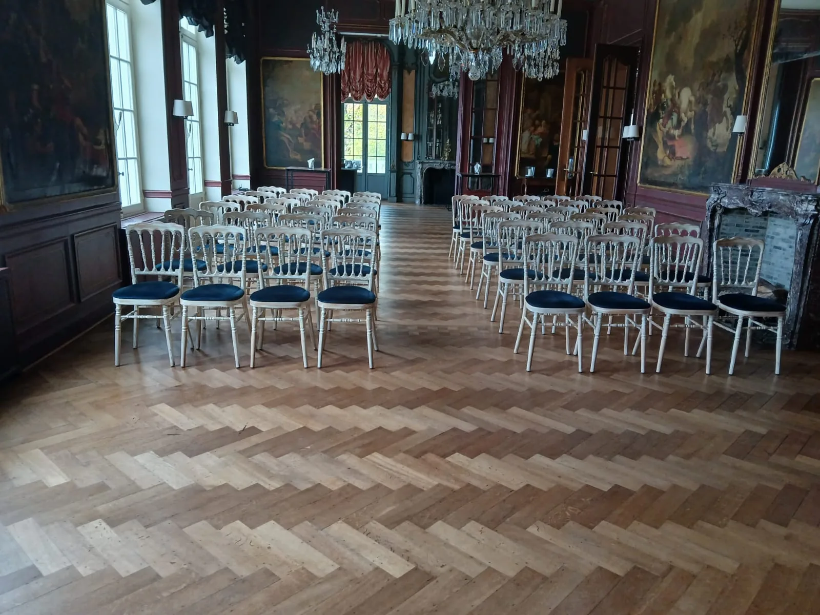 Salle de réception avec parquet en chevrons et chaises argentées alignées le long des murs